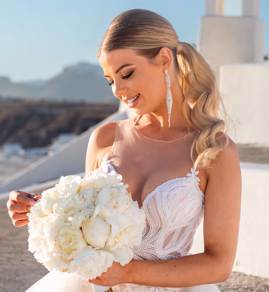 Wedding in Greece. Santorini. A shot of the bride in a wedding dress looking at the bouquet of flowers held in her hands.