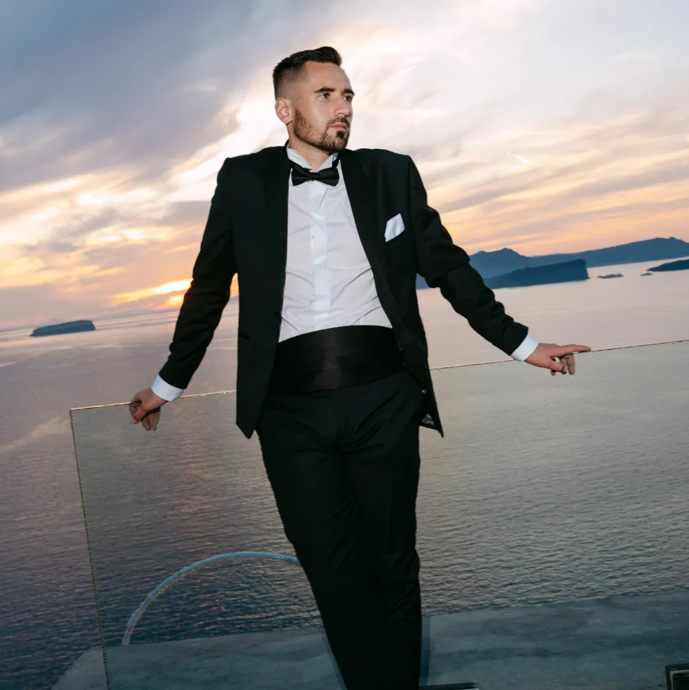 A wedding in Greece, Santorini. A shot of the groom in his wedding suit standing on the terrace.